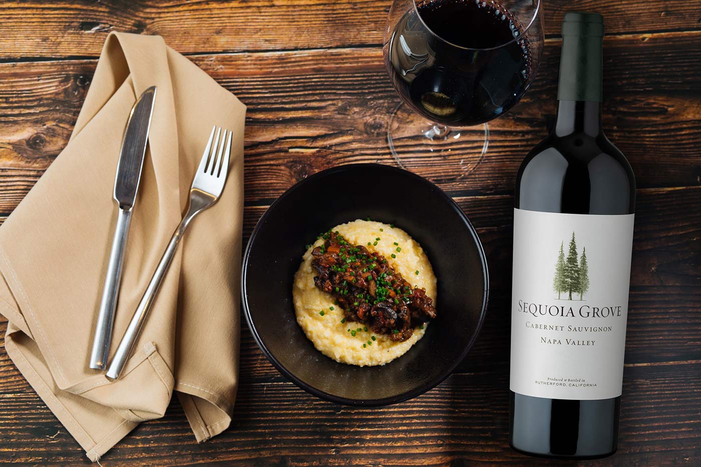 Bolognese over Polenta on a plate next to a bottle of Sequoia Grove Napa Valley Cabernet Sauvigon red wine