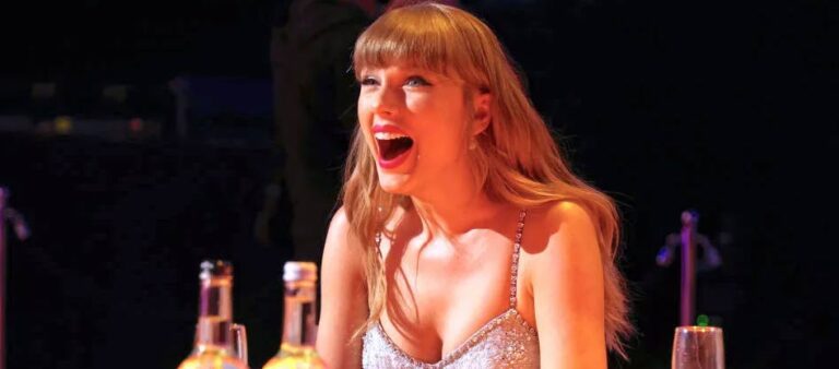 Taylor Swift laughing with a bottle of wine in front of her