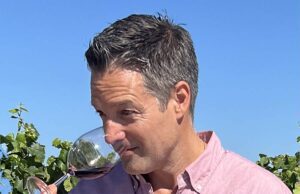 Wine Educator Nick Poletto dipping his nose into a wine glass to smell red wine with a vineyard in the background